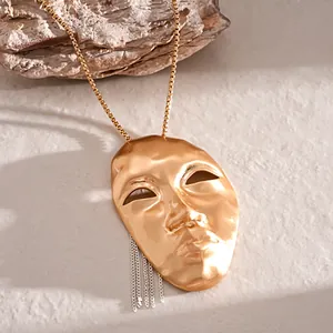 Close-up of an artistic gold human mask pendant featuring a silver chain tassel detail