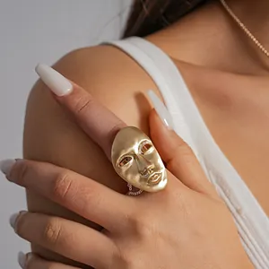 Detail view of an avant-garde golden human face mask ring showing artistic metallic textures.