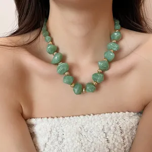 Détail d'un collier en perles d'acrylique marbré vert avec entretoises dorées sur modèle.