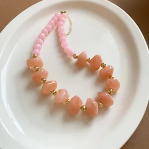 Vue détaillée d'un collier de perles en acrylique rose et pêche présenté sur un plat blanc.