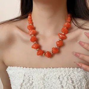 Détail d'un collier de perles en acrylique orange vif avec séparateurs dorés