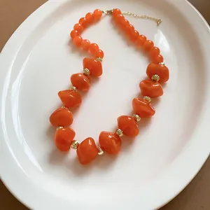 Détail des perles acryliques orange vif et des accents dorés sur ce collier ras-du-cou chic