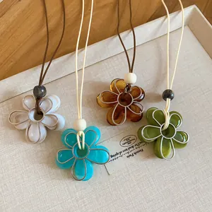 Détail rapproché de colliers avec pendentifs fleurs en résine colorée et cordons.