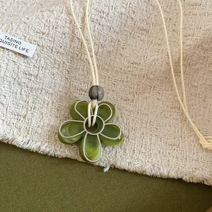 Gros plan détaillé d'un collier pendentif fleur en résine verte sur fond de tissu