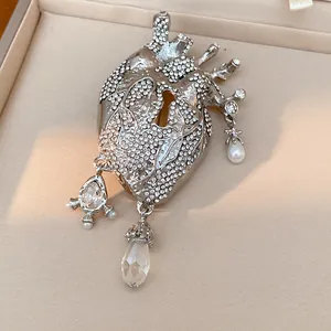 Macro view of a silver rhinestone anatomical heart brooch with keyhole and pearl charms.