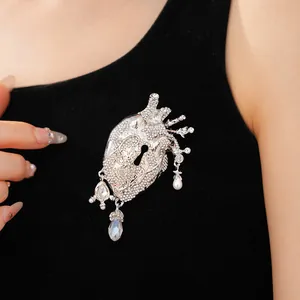Macro detail view of a silver anatomical heart brooch with crystals and pearl on black