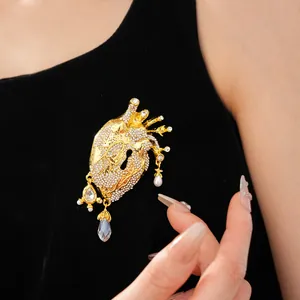 Close-up of gold anatomical heart brooch with pavé rhinestones and pearl dangles.