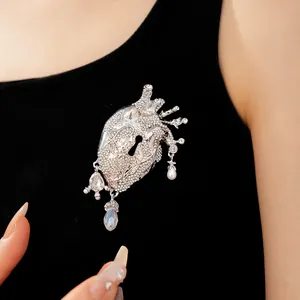 Close-up of a silver rhinestone anatomical heart brooch with keyhole detail on black fabric