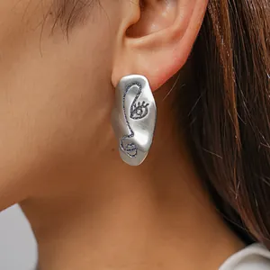 Close-up of matte silver stud earring with artistic abstract face design