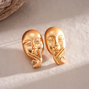 Detailed macro view of gold matte portrait mask stud earrings with unique hand gesture