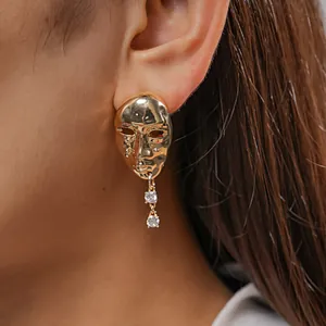 Close-up of gold-plated human mask stud earring with crystal drops on model's ear