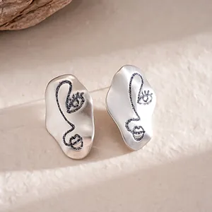 Close-up of minimalist matte silver earrings with abstract black glitter face design