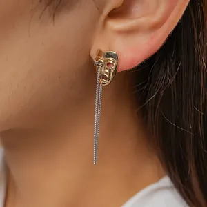 Close-up detail showing the unique gold mask earring design with elegant silver chain tassel.
