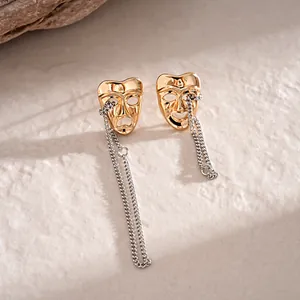 Detailed view of gold mask earrings with dangling silver chains on stone background