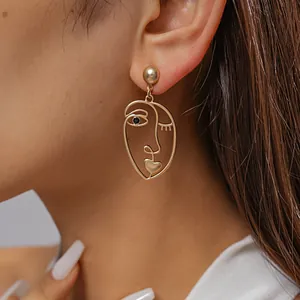 Detailed close-up showing a matte gold abstract face mask earring on a model's ear
