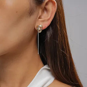 Close-up view of creative gold mask earring featuring a delicate silver hanging chain