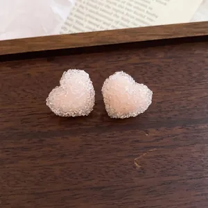 Zoete roze hars hartvormige oorknopjes met zilveren naalden op een houten blad