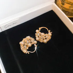 Detailansicht goldener Korb-Ohrringe mit weißen Perlen und glitzernden Strasssteinen