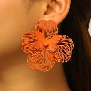 Close-up detail of oversized orange hollow-out flower earring with butterfly center