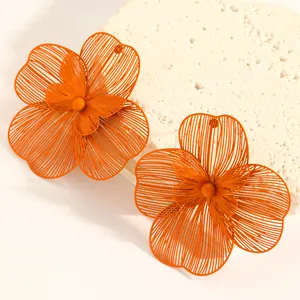 Macro detail of oversized orange hollow flower earrings with a layered petal design