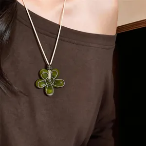 Vue détaillée d'un collier avec pendentif fleur en résine verte porté sur un haut marron.