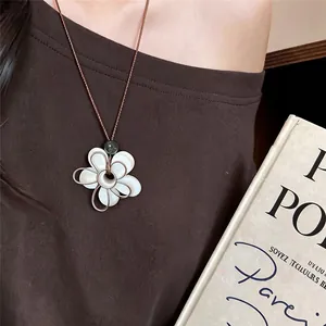 Gros plan d'un pendentif fleur en résine blanche avec un cordon marron minimaliste