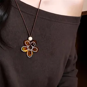 Détail d'un collier fleur en résine ambrée porté avec un haut marron à épaules dénudées.