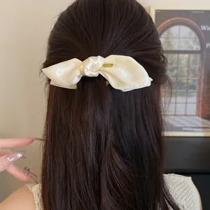 Detailed view of a cream satin bow hair clip styled on dark brown hair