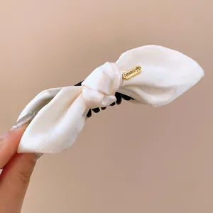 Close-up view of a cream fabric bow hair claw clip with a gold 'classic' metal tag