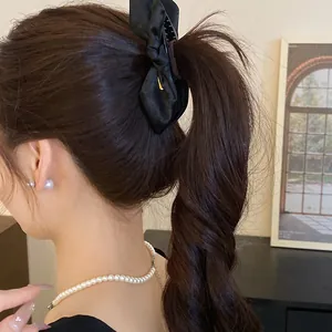 Elegant black satin bow hair clip styled on a brunette ponytail with pearl necklace