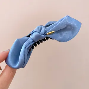 Detailed view of the blue satin bow hair claw clip with a decorative gold metal tag