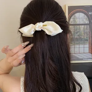 Detail view of an elegant cream satin bow hair clip styled on long dark wavy hair