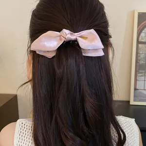 Elegant pink satin bow hair clip accessory presented on a model with long wavy brown hair