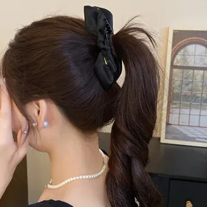 Close-up detail of an elegant black satin bow hair claw clip styled in a low ponytail.