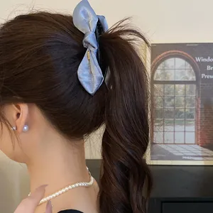 Detail view of a blue satin bow hair claw clip styled in a high wavy ponytail.