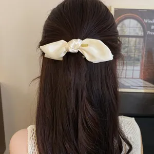 Detail view of a cream satin bow hair clip styled in dark brown hair for a sweet look
