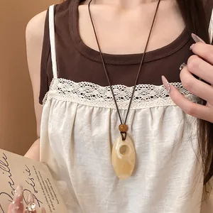 Primo piano di una collana bohémien con ciondolo ovale in resina e cordino in cuoio marrone