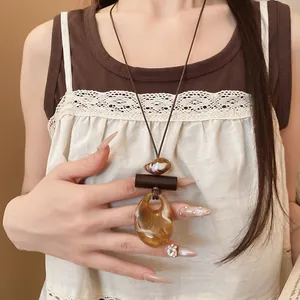 Dettaglio di una collana con ciondolo ovale in resina bohémien su cordino marrone.