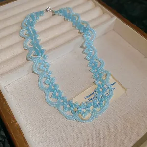 Close-up of a blue beaded lace necklace with heart-like patterns in a display tray.