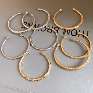 Detailopname van gouden en zilveren open armbanden met verschillende texturen op grijs.