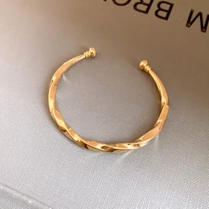 Gedetailleerd vooraanzicht van een elegante goudkleurige gedraaide metalen open armband