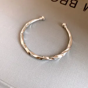 Detailopname van een zilveren gedraaide metalen manchetarmband met gepolijste afwerking en open design