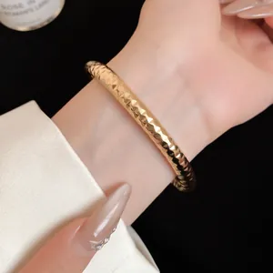 Gedetailleerde close-up van een goudkleurige metalen open armband met gehamerde textuur