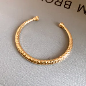Gedetailleerde macro-opname van een gouden getextureerde open armband met bollen