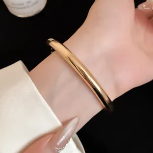 Detailopname van een minimalistische goudkleurige gladde ronde open metalen armband om pols.