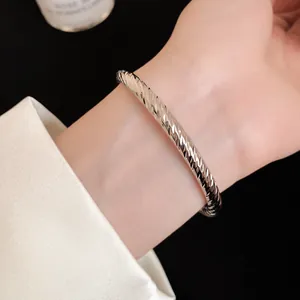 Detailopname van een zilveren getextureerde metalen armband om de pols van een vrouw.