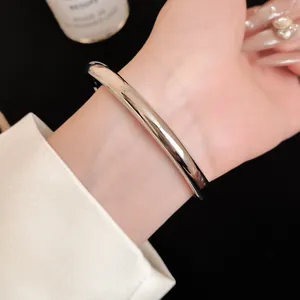 Detailopname van een gepolijste zilveren metalen open armband om een vrouwelijke pols
