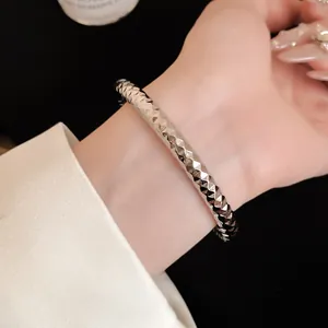 Detailopname van een zilverkleurige metalen armband met een gefacetteerde textuur
