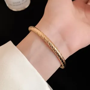 Detailopname van een gouden open armband met elegante diamantgeslepen patronen aan de pols