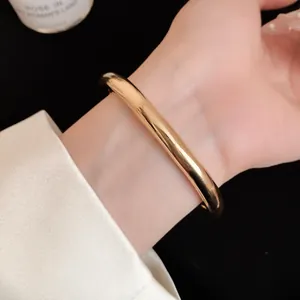 Detailopname van een elegante gouden metalen gladde ronde open armband om de pols gedragen
